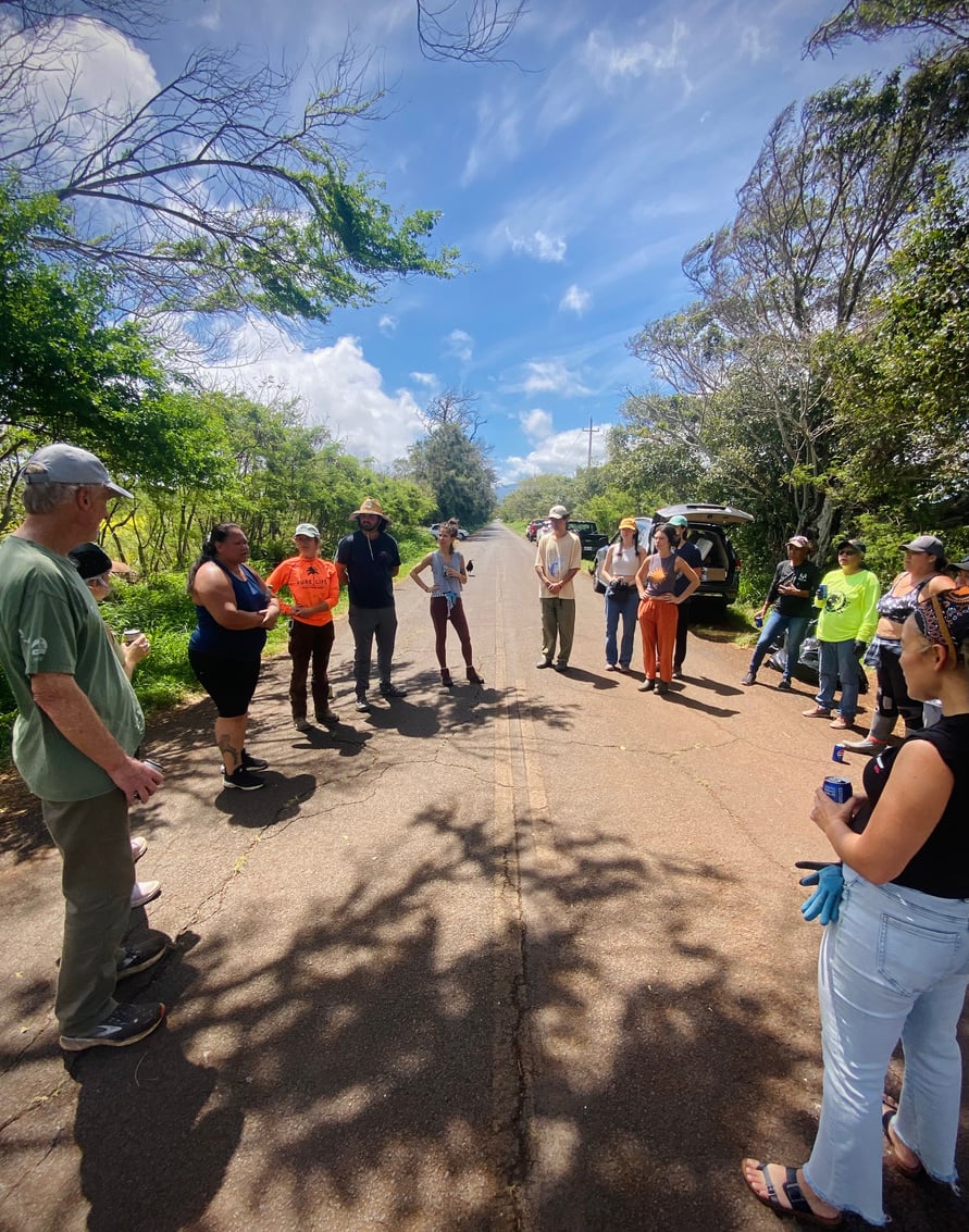 Volunteers gathered in the road for a cleanup briefing under a bright blue sky