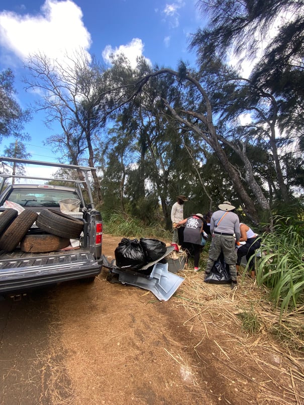 A pickup carrying discarded tires while volunteers collect more roadside waste