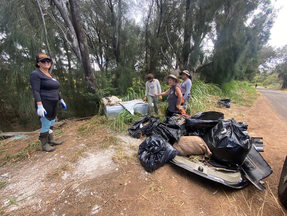 Volunteers standing beside bags of trash and a discarded vehicle panel