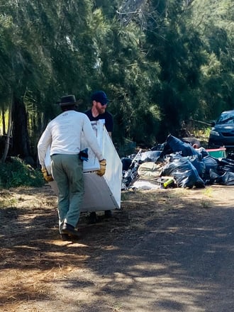 A volunteer carrying a discarded appliance toward a cleanup collection pile