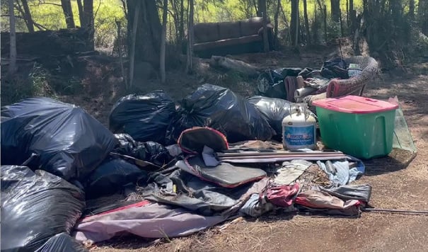 Collected furniture, bags, containers, and household debris beside Holomua Road