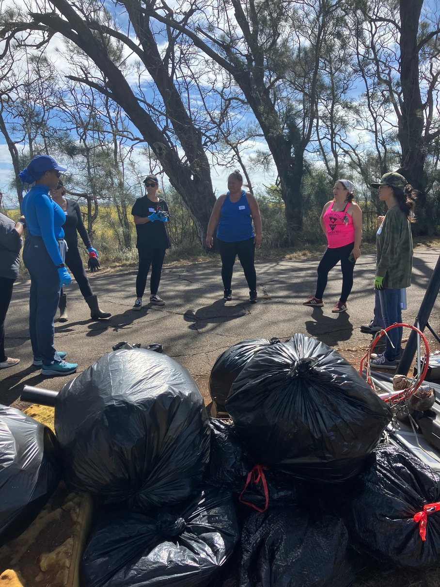Volunteers meeting beside a large collection of bagged waste on Holomua Road