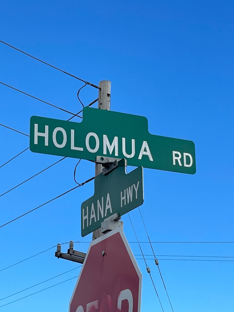 Holomua Road and Hāna Highway street signs against a clear blue sky