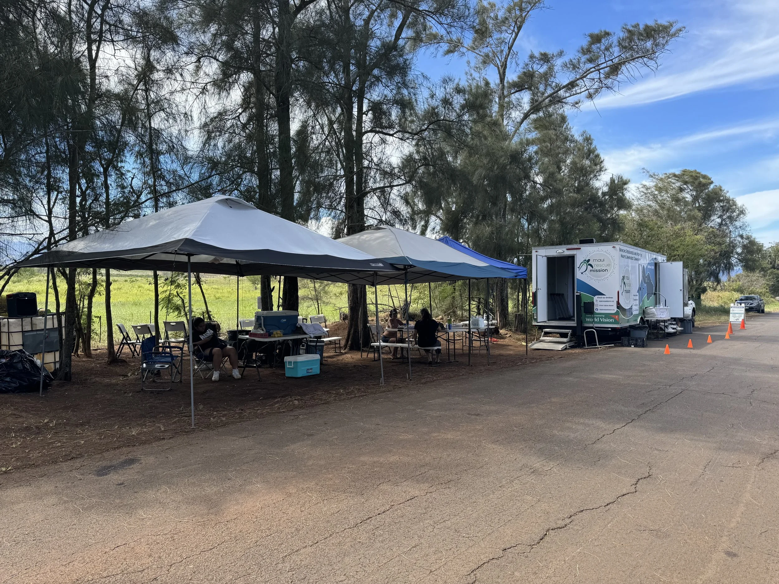 A mobile outreach site with shade tents, tables, and a Maui Rescue Mission vehicle